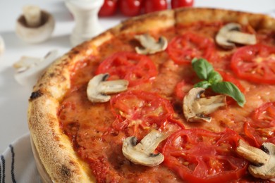 Delicious pizza with tomatoes, mushrooms and basil on table, closeup