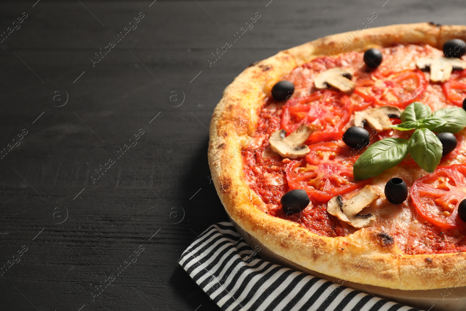 Photo of Delicious pizza with tomatoes, mushrooms, olives and basil on black wooden table, closeup