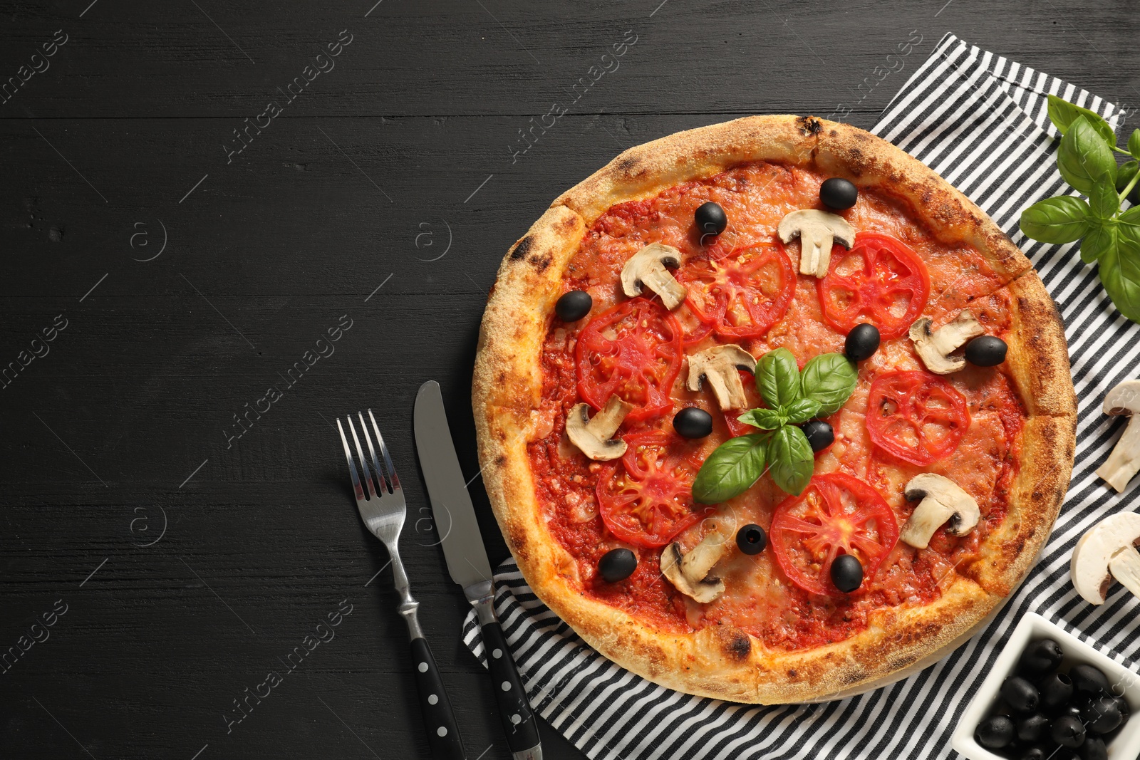 Photo of Delicious pizza with tomatoes, mushrooms, olives and basil served on black wooden table, flat lay. Space for text