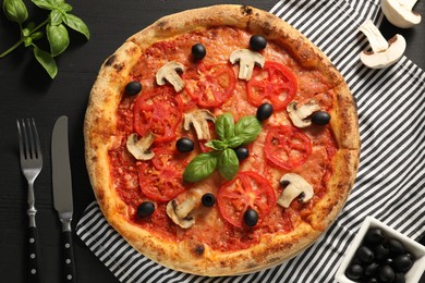 Delicious pizza with tomatoes, mushrooms, olives and basil served on black wooden table, flat lay