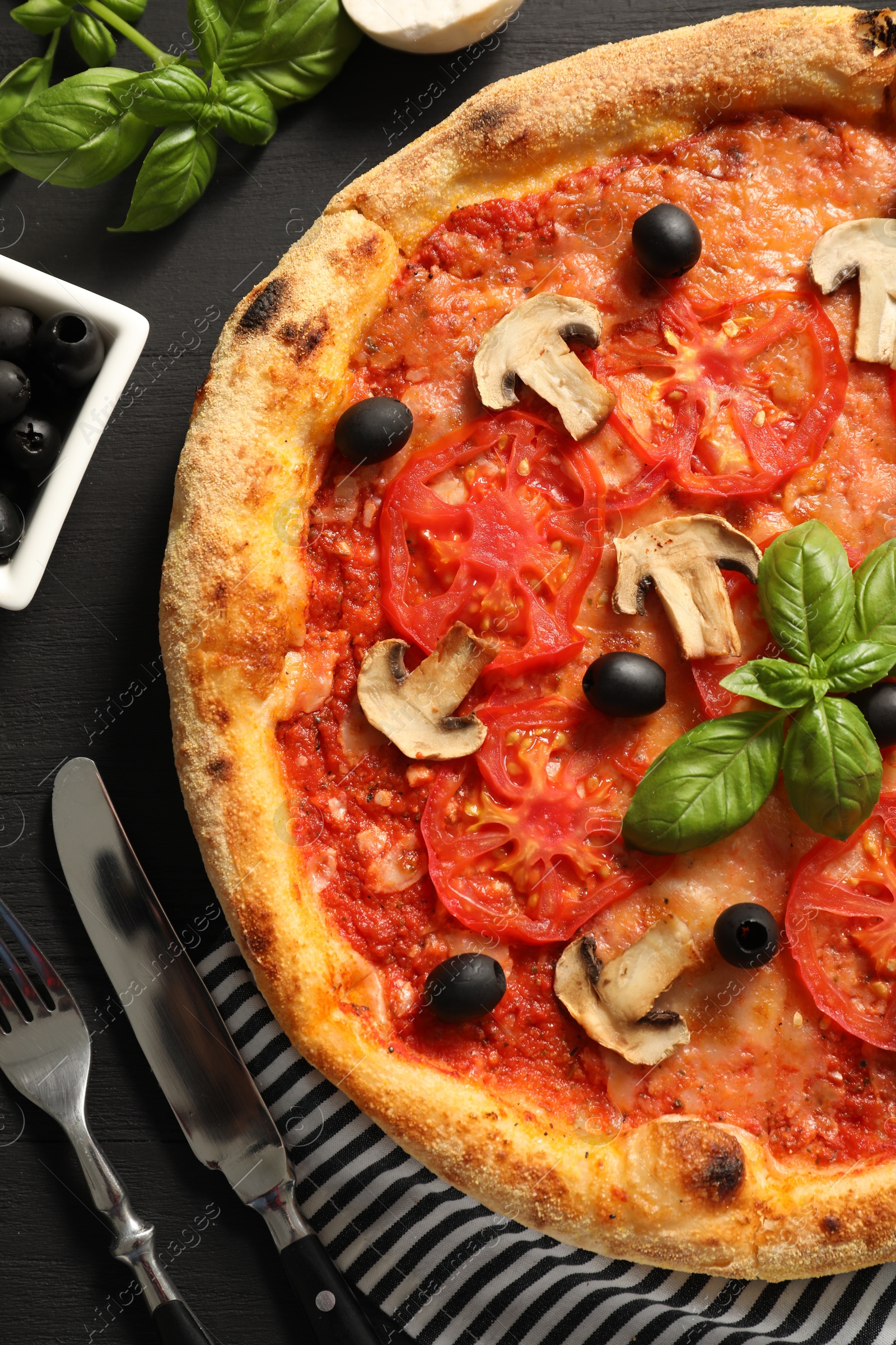 Photo of Delicious pizza with tomatoes, mushrooms, olives and basil served on black wooden table, flat lay