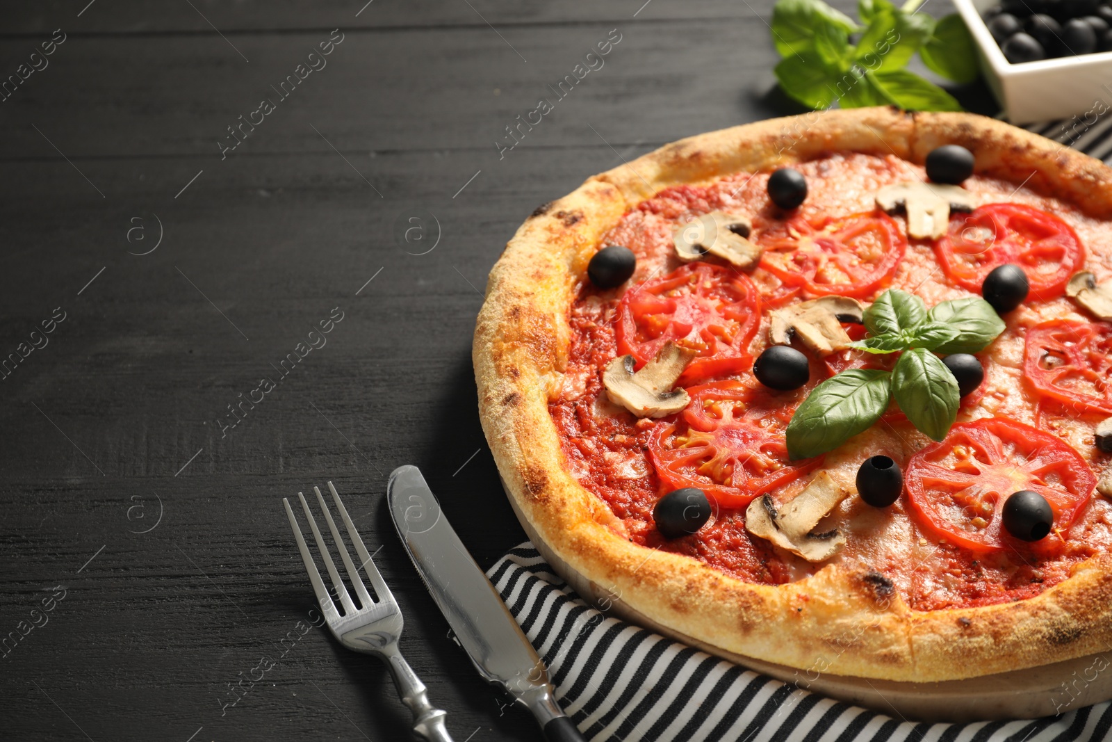 Photo of Delicious pizza with tomatoes, mushrooms, olives and basil served on black wooden table, closeup