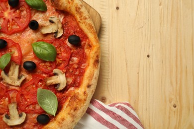 Delicious pizza with tomatoes, mushrooms, black olives and basil on wooden table, top view. Space for text