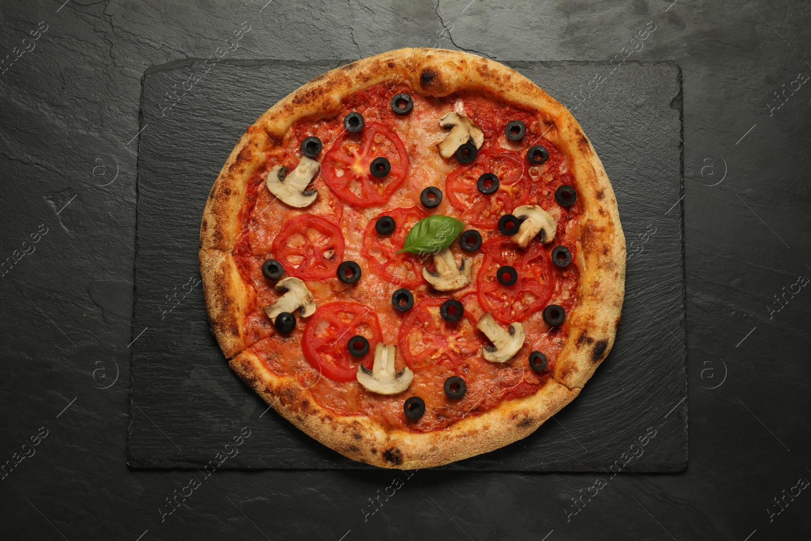 Photo of Delicious pizza with tomatoes, mushrooms, olives and basil on black textured table, top view