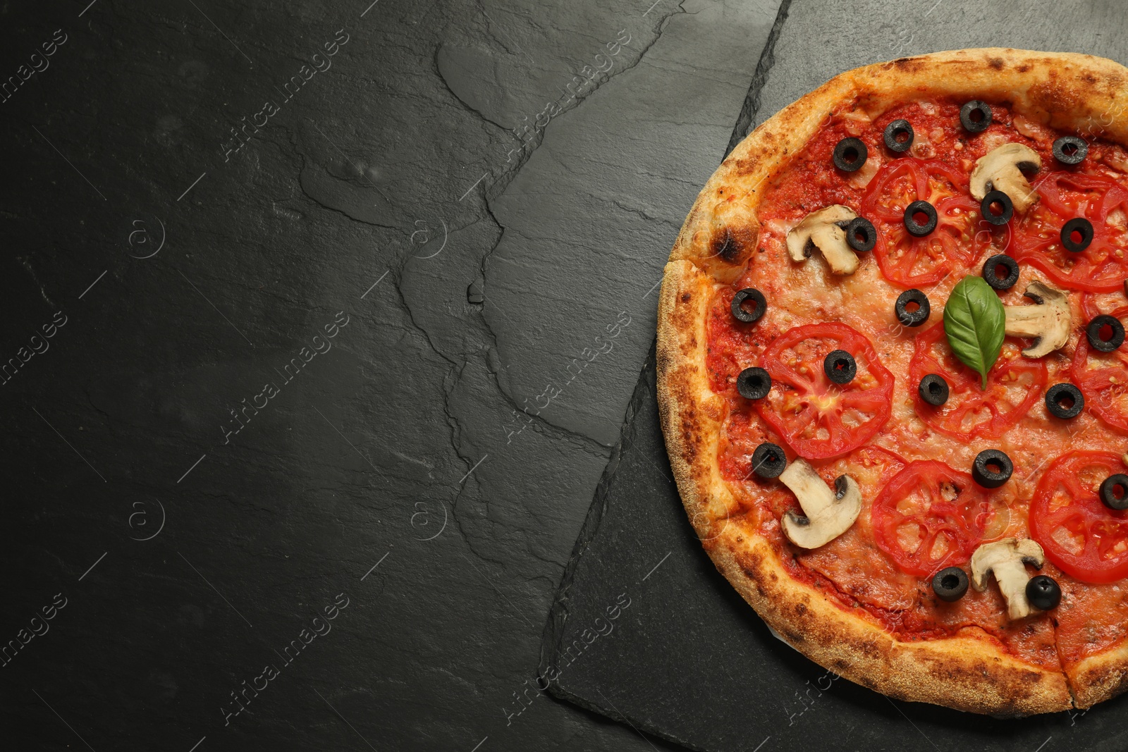 Photo of Delicious pizza with tomatoes, mushrooms, olives and basil on black textured table, top view. Space for text