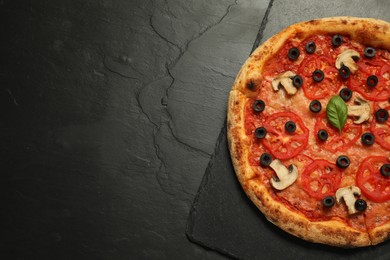 Delicious pizza with tomatoes, mushrooms, olives and basil on black textured table, top view. Space for text