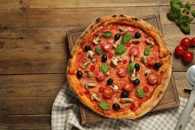 Delicious pizza with tomatoes, mushrooms, black olives and basil on wooden table, flat lay. Space for text