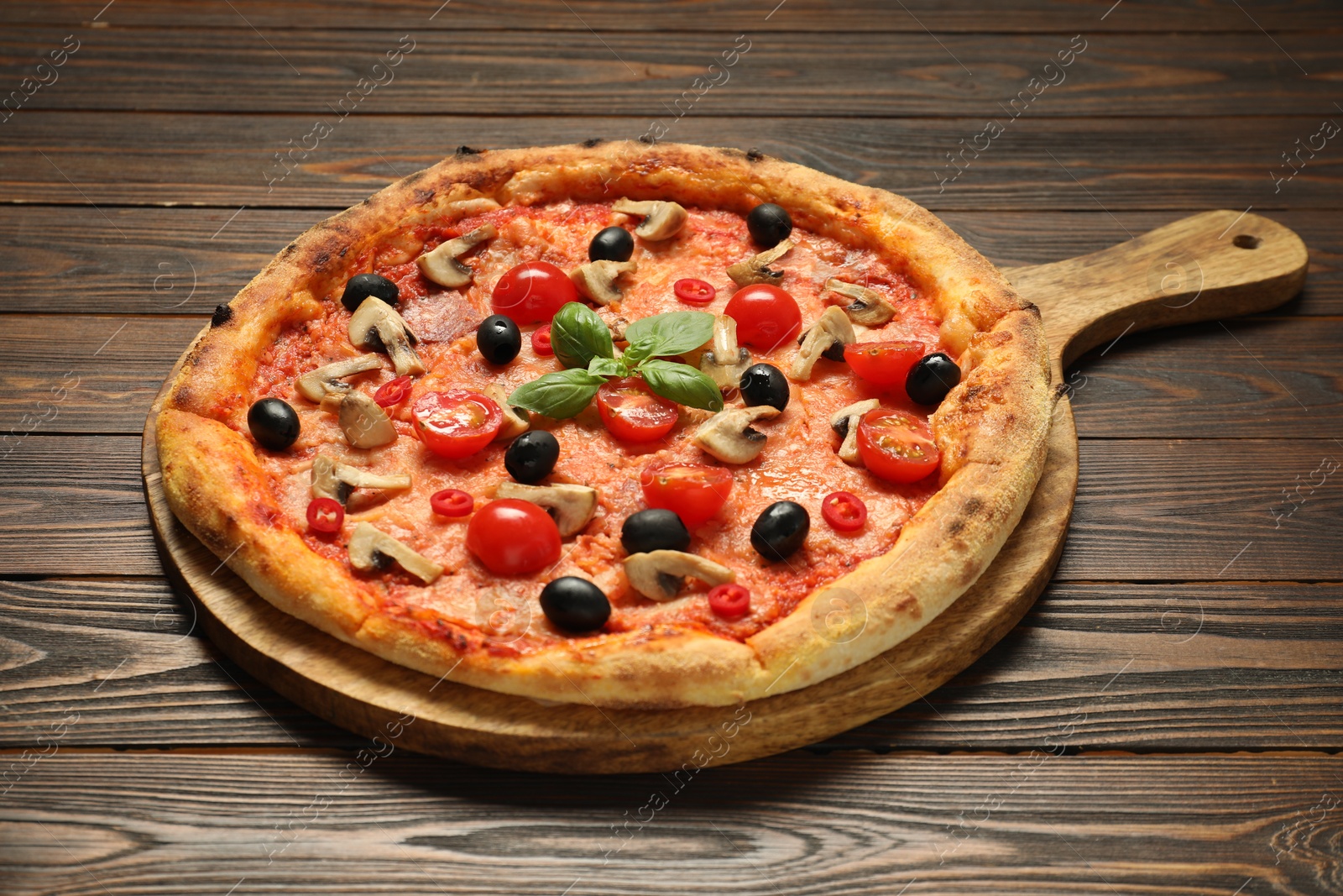 Photo of Delicious pizza with tomatoes, mushrooms, black olives and basil on wooden table