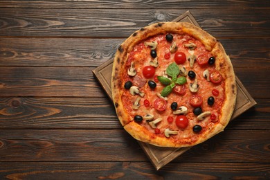 Delicious pizza with tomatoes, mushrooms, black olives and basil on wooden table, top view. Space for text