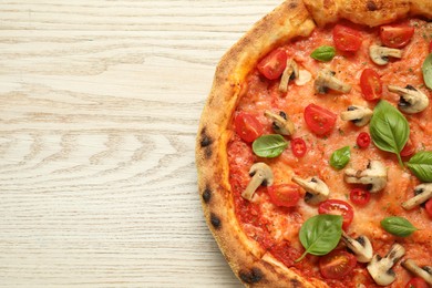 Delicious pizza with tomatoes, mushrooms and basil on wooden table, top view. Space for text