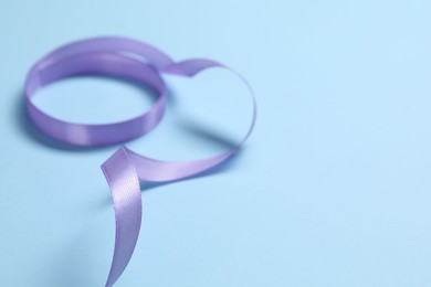 Photo of Beautiful violet ribbon on light blue background, closeup. Space for text