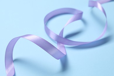 Photo of Beautiful violet ribbon on light blue background, closeup