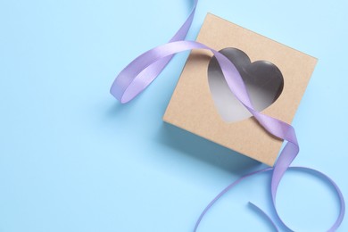 Photo of Beautiful violet ribbon and gift box with heart on light blue background, flat lay. Space for text