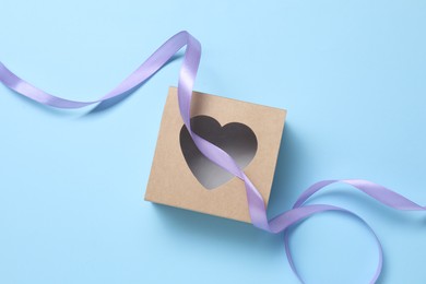 Photo of Beautiful violet ribbon and gift box with heart on light blue background, flat lay