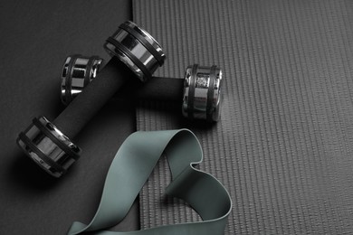 Dumbbells, yoga mat and fitness elastic band on black background, above view. Space for text