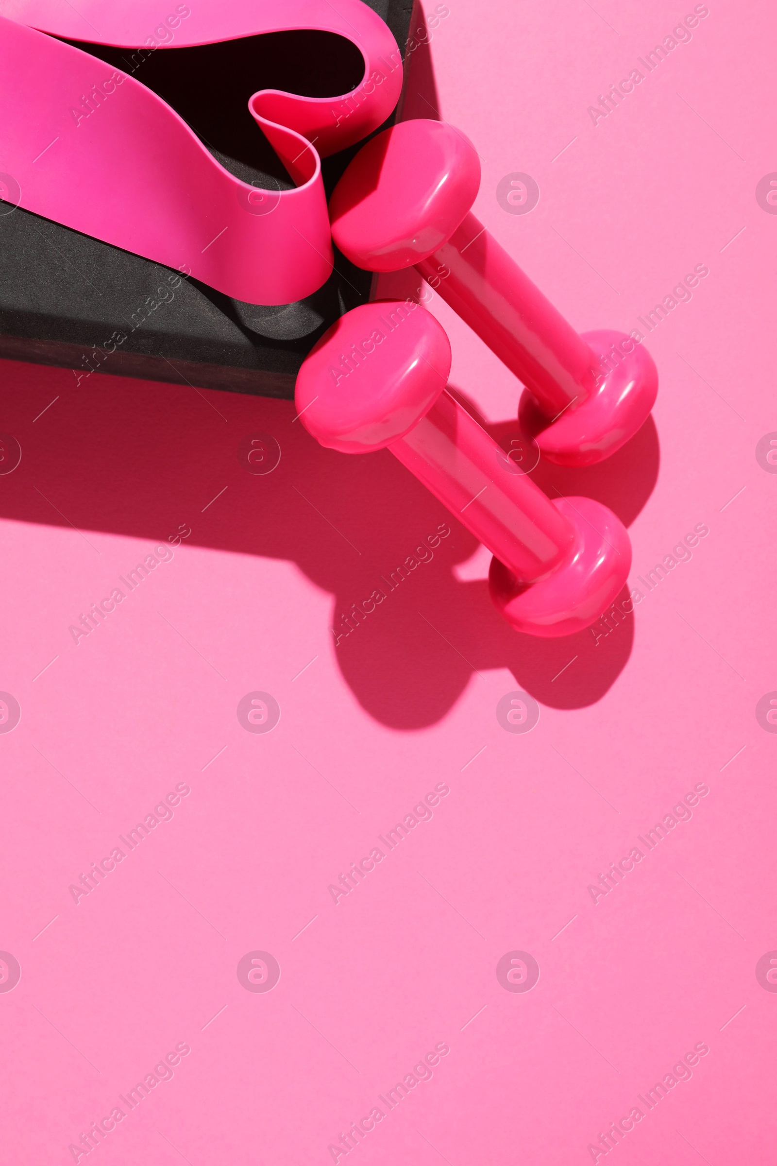 Photo of Dumbbells, fitness elastic band and yoga block on pink background, flat lay. Space for text