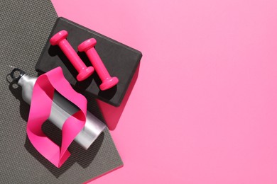 Dumbbells and other sports equipment on pink background, flat lay. Space for text