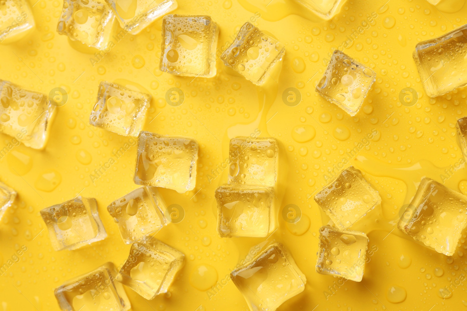 Photo of Crystal clear ice cubes on yellow background, flat lay