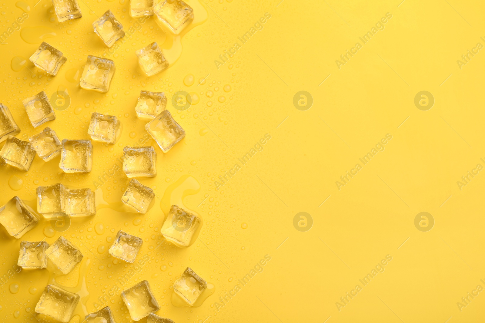 Photo of Crystal clear ice cubes on yellow background, flat lay. Space for text