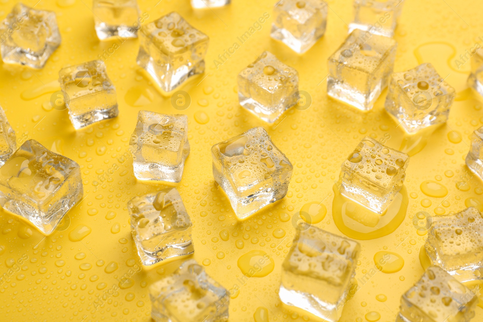Photo of Crystal clear ice cubes on yellow background, closeup