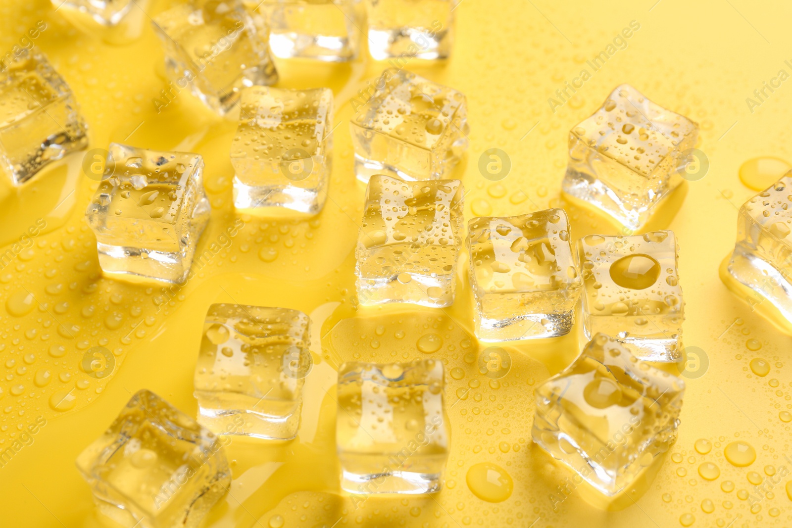 Photo of Crystal clear ice cubes on yellow background, closeup