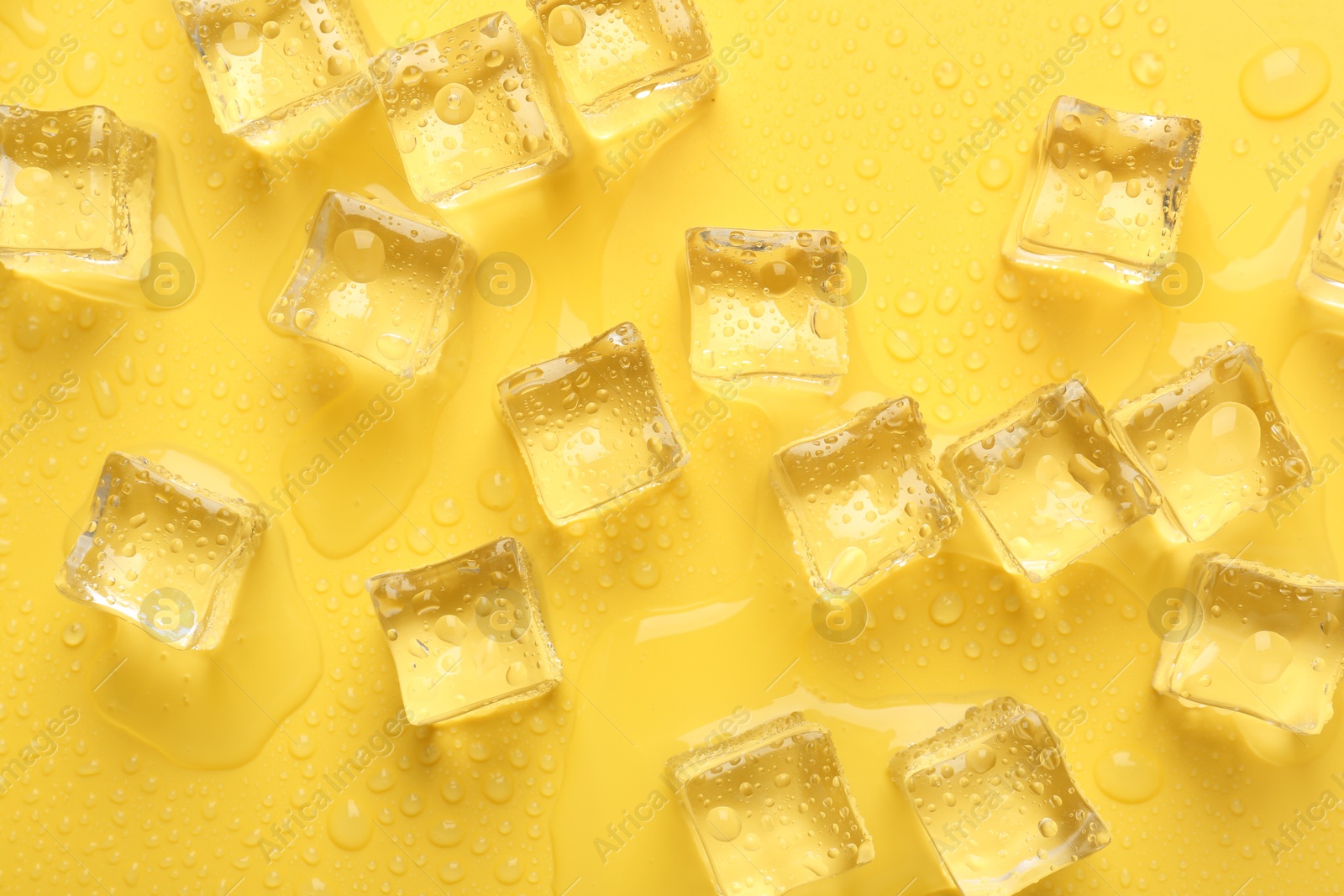 Photo of Crystal clear ice cubes on yellow background, flat lay