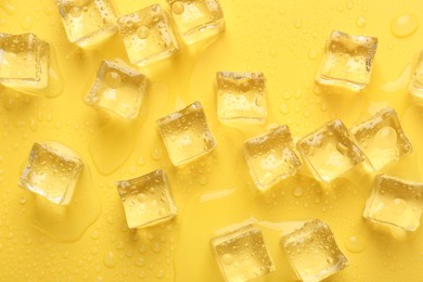 Crystal clear ice cubes on yellow background, flat lay