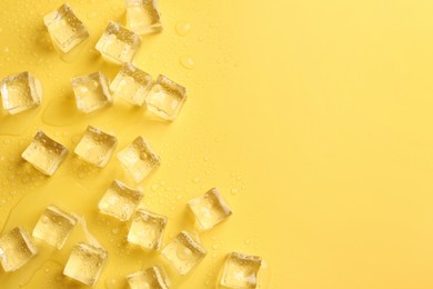 Photo of Crystal clear ice cubes on yellow background, flat lay. Space for text