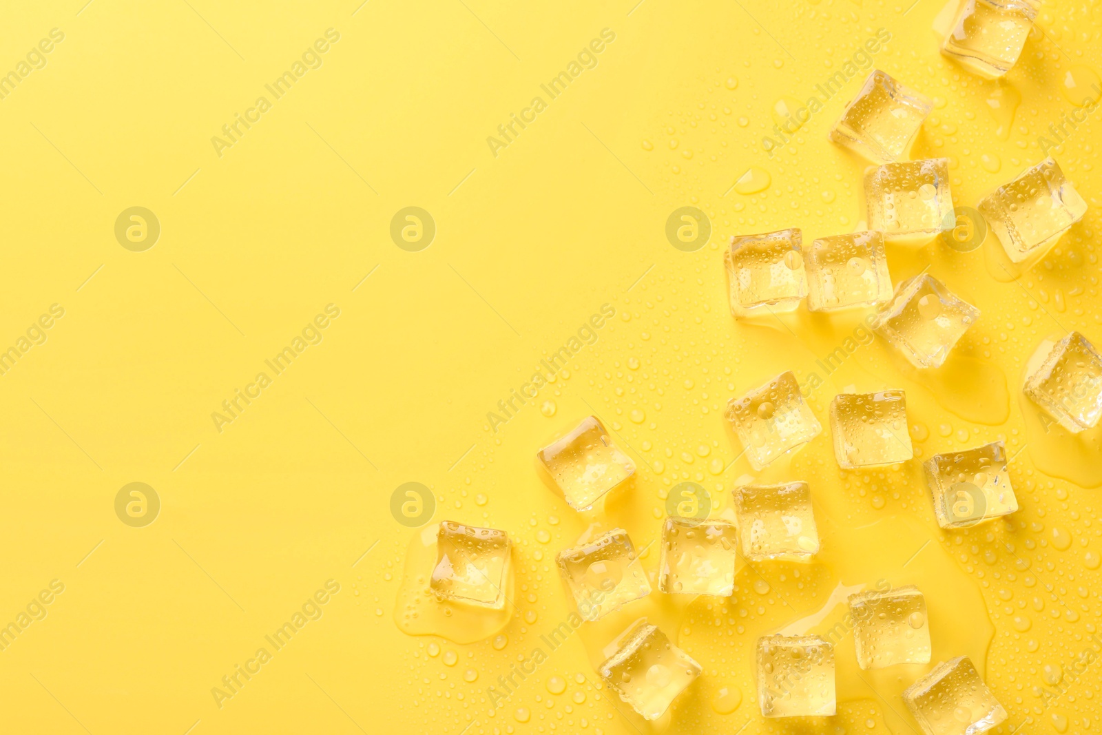 Photo of Crystal clear ice cubes on yellow background, flat lay. Space for text