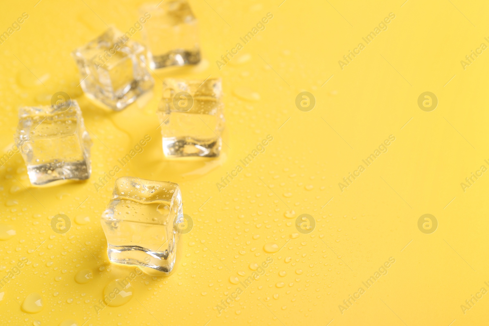 Photo of Crystal clear ice cubes on yellow background, closeup. Space for text