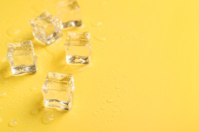 Crystal clear ice cubes on yellow background, closeup. Space for text