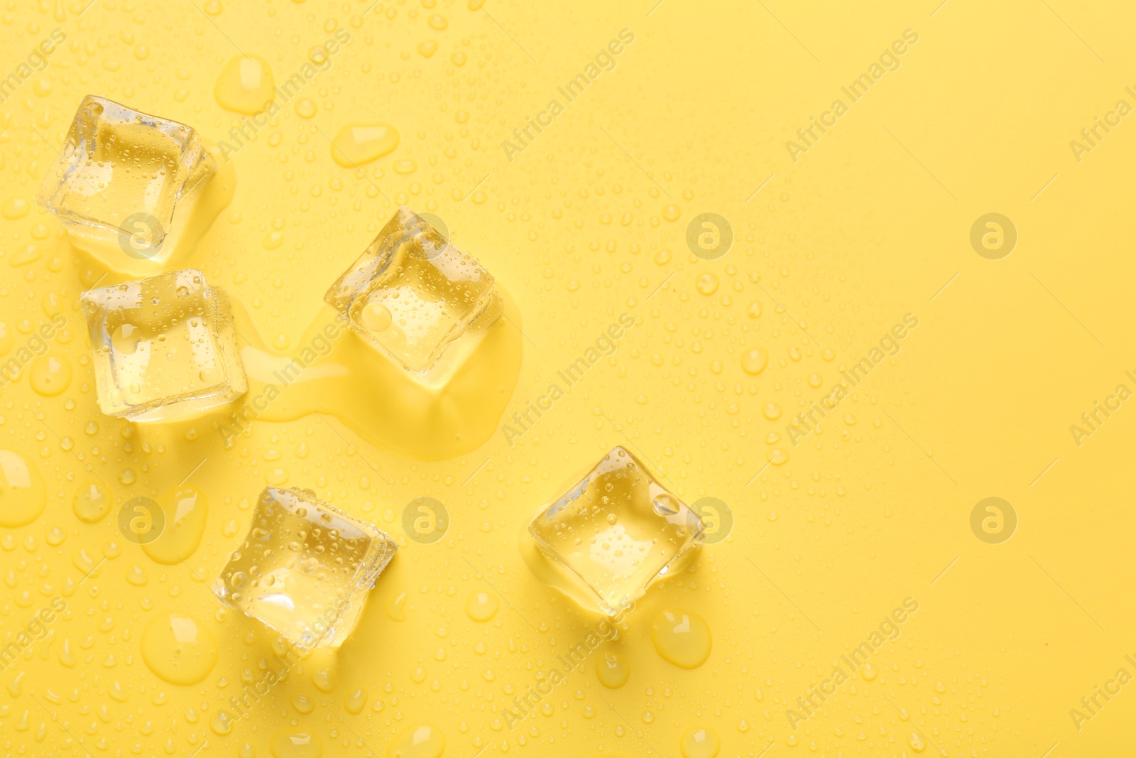 Photo of Crystal clear ice cubes on yellow background, flat lay. Space for text