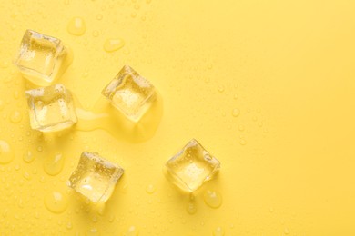 Crystal clear ice cubes on yellow background, flat lay. Space for text