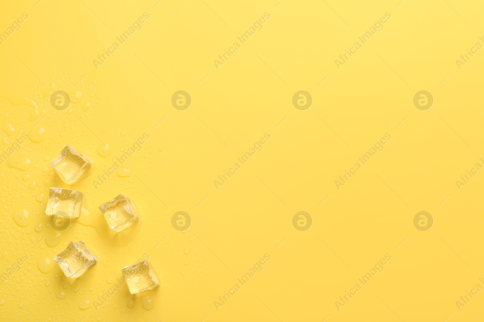 Photo of Crystal clear ice cubes on yellow background, flat lay. Space for text