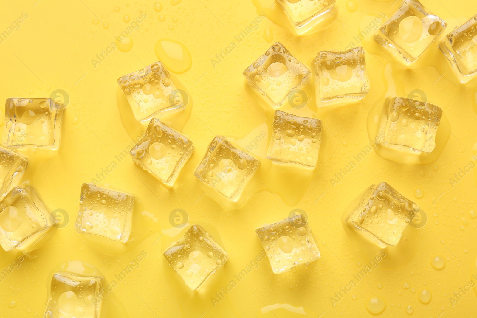 Photo of Crystal clear ice cubes on yellow background, flat lay