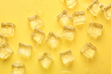 Crystal clear ice cubes on yellow background, flat lay