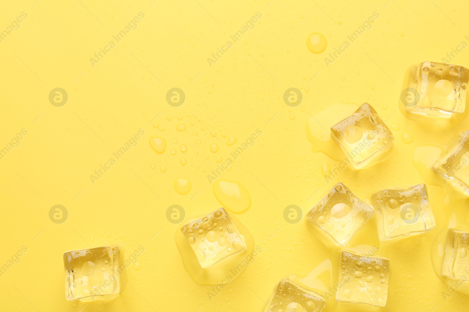 Photo of Crystal clear ice cubes on yellow background, flat lay. Space for text