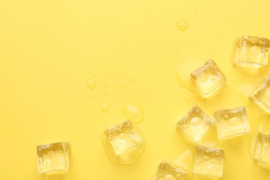 Crystal clear ice cubes on yellow background, flat lay. Space for text