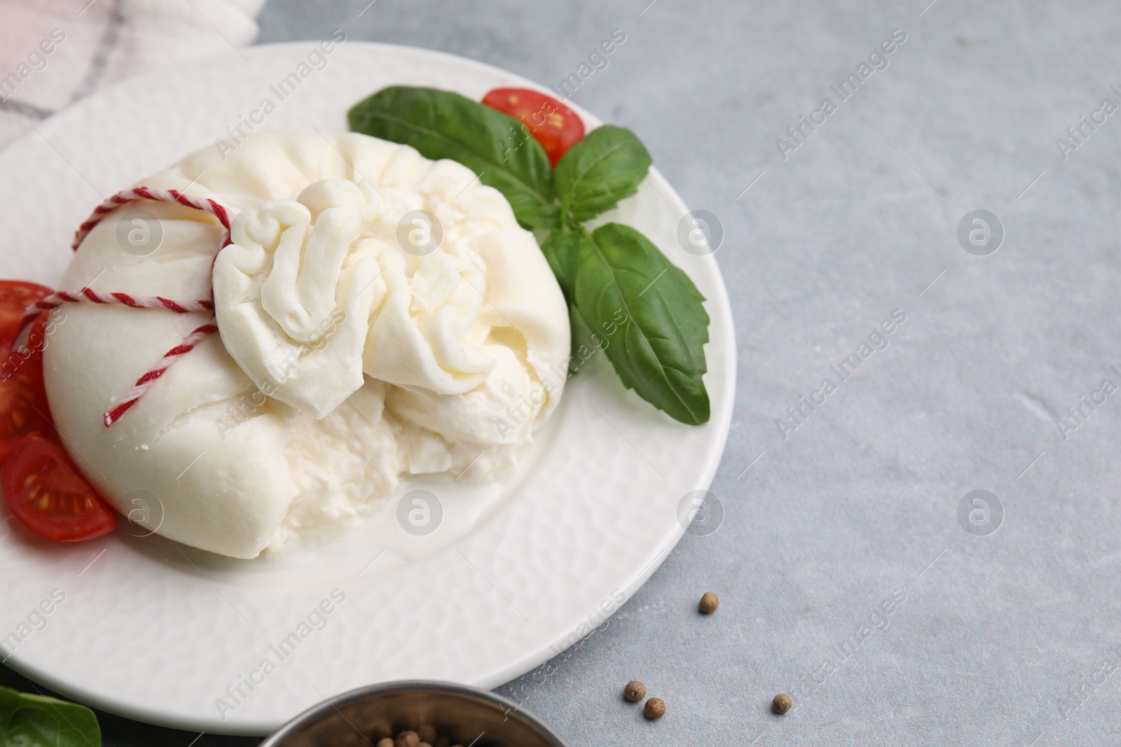 Photo of Delicious fresh burrata cheese with tomato and basil on grey table, space for text