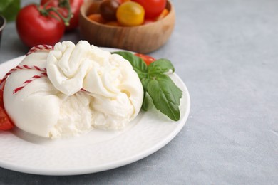 Photo of Delicious fresh burrata cheese with basil leaves on grey table, space for text