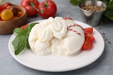 Photo of Delicious fresh burrata cheese with basil leaves and tomato on grey table