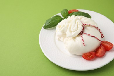 Photo of Delicious fresh burrata cheese with basil leaves and tomato on green table. Space for text