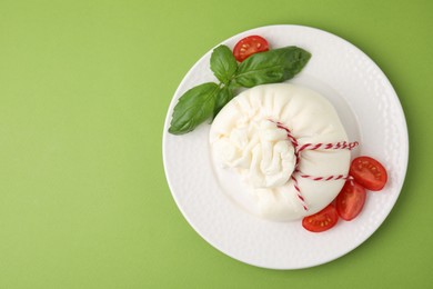 Delicious fresh burrata cheese with basil and tomato on green table, top view. Space for text