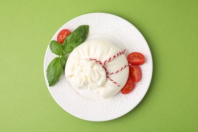 Photo of Delicious fresh burrata cheese with basil leaves and tomato on green table, top view