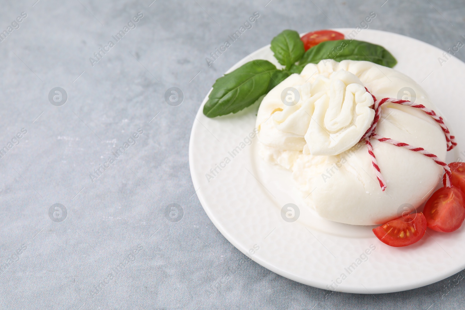 Photo of Delicious fresh burrata cheese with basil leaves and tomato on grey table, space for text