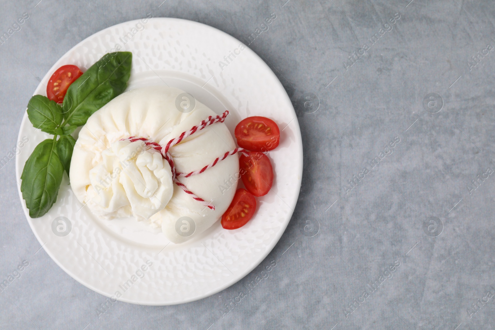 Photo of Delicious fresh burrata cheese with basil and tomato on grey table, top view. Space for text