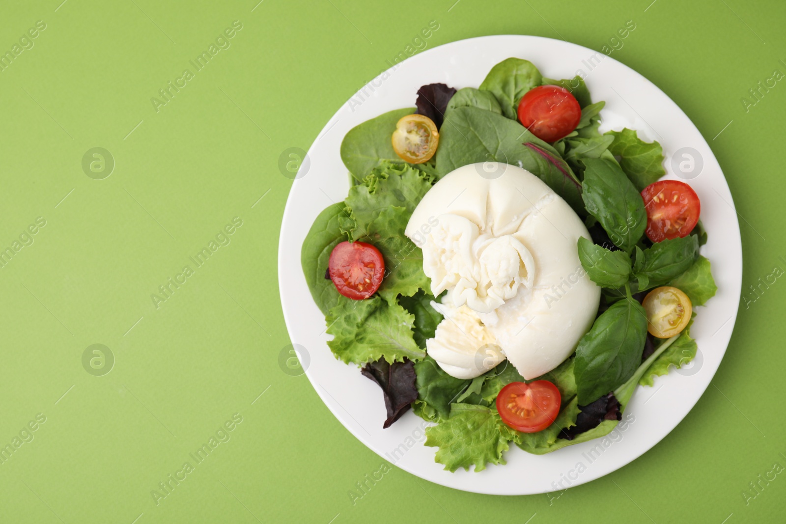 Photo of Delicious fresh burrata salad on green table, top view. Space for text