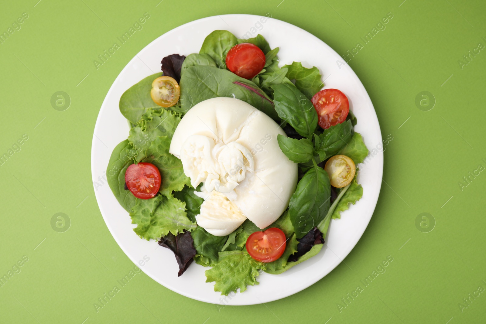 Photo of Delicious fresh burrata salad on green table, top view