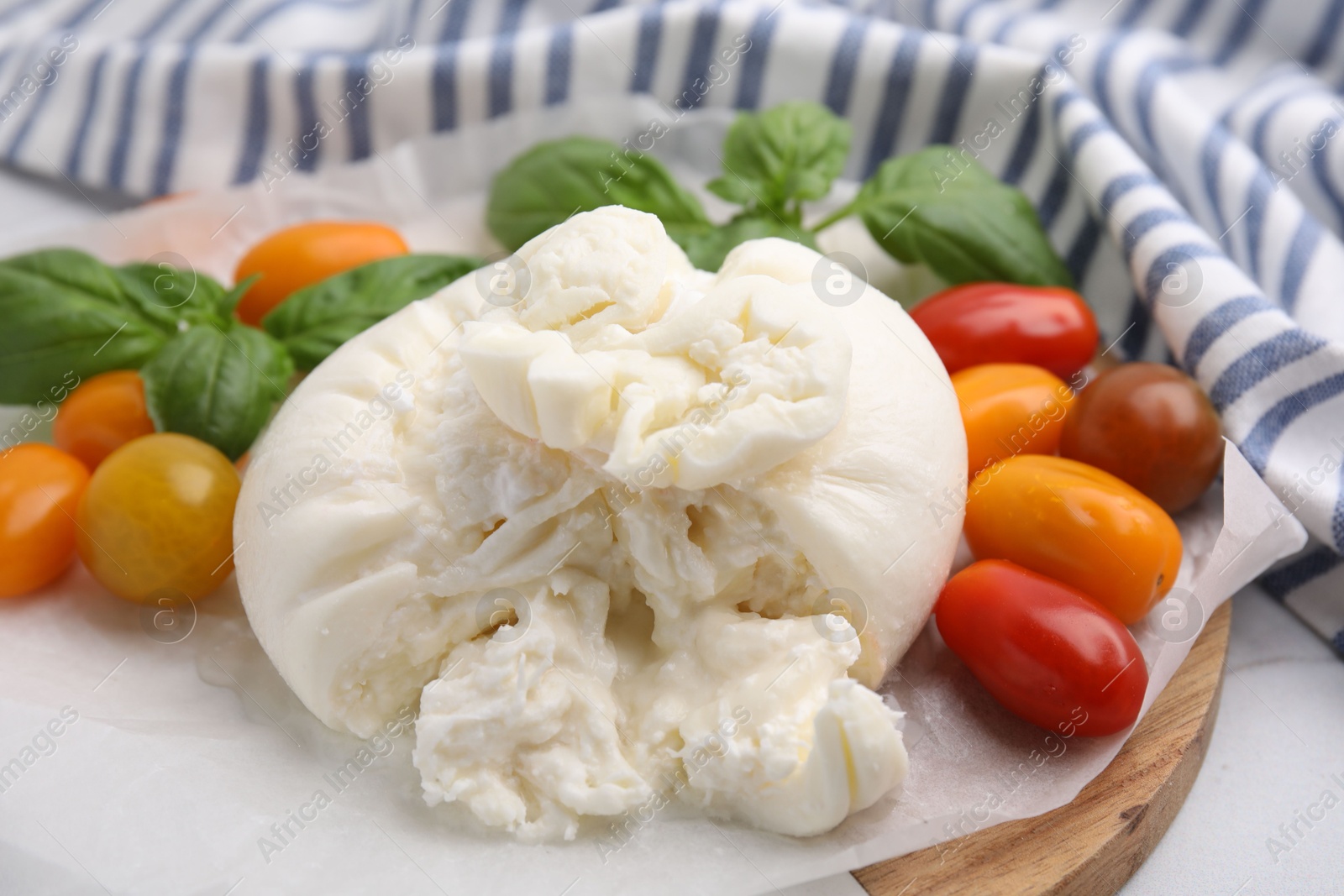 Photo of Delicious fresh burrata cheese with basil leaves and tomatoes on white table, closeup