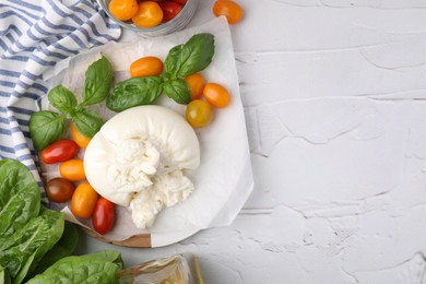 Photo of Delicious fresh burrata cheese with basil leaves and tomatoes on white textured table, flat lay. Space for text